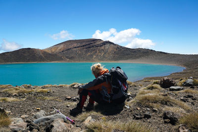 Backpacker sitting at lakeshore against sky