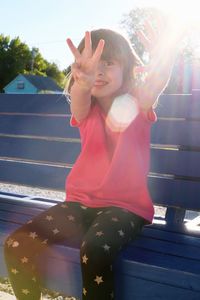 Cute smiling girl gesturing on bench during sunny day