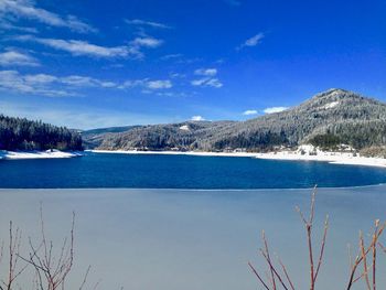 Scenic view of lake by snowcapped mountains against blue sky