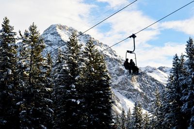 Low angle view of silhouette people traveling in ski lift against snow covered mountains
