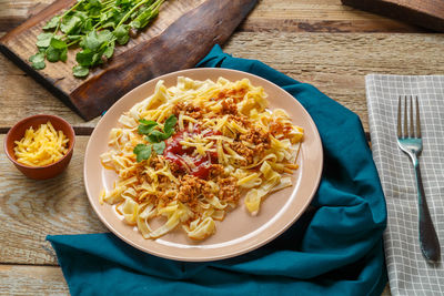 Pasta bolognese garnished with herbs and cheese in a plate on a blue napkin on a wooden table