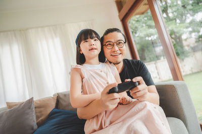 Smiling father and daughter playing video game at home