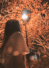 Low angle view of woman standing against illuminated street light at night