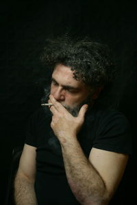Midsection of man smoking cigarette against black background
