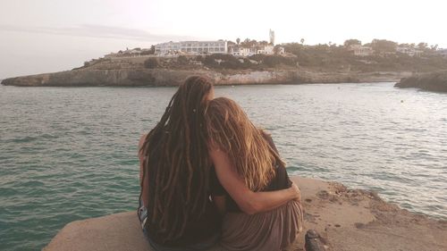 Rear view of couple sitting on pier by lake