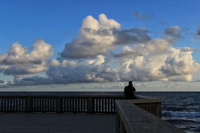 Rear view of man sitting on pier over sea against sky