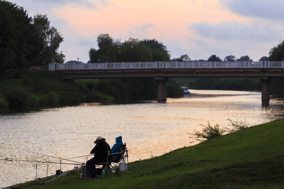 People on bridge over river against sky