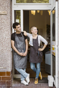 Male and female owners looking away while standing at cafe doorway