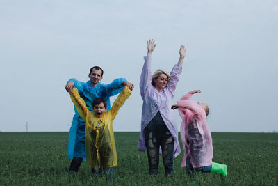 Happy family with arms raised standing on field against sky