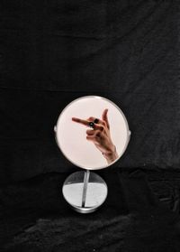 Reflection of hand showing obscene gesture in mirror against black backdrop