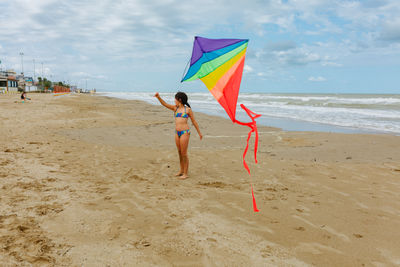 Rear view of woman walking at beach against sky