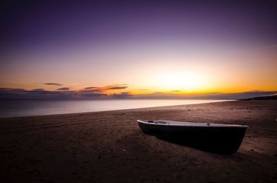 Boat moored on beach against clear sky during sunset