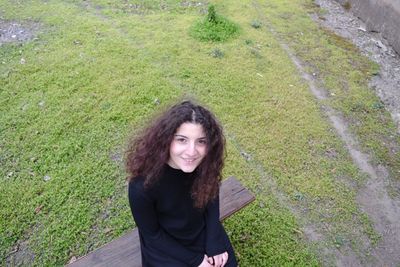 Portrait of smiling young woman sitting on bench at park