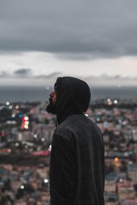 Side view of man wearing hood against cityscape
