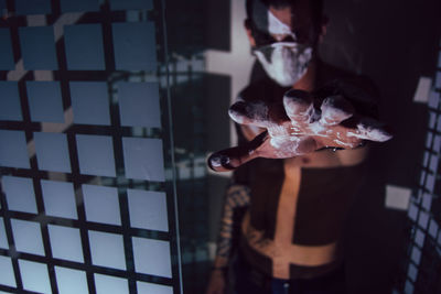 Portrait of young man wearing mask standing by window in darkroom