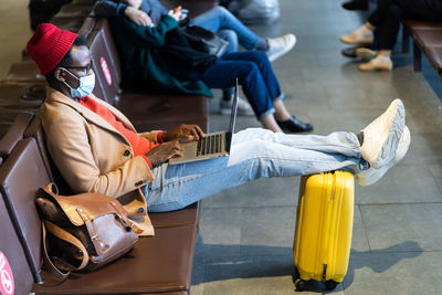 Young businessman wearing mask using laptop while sitting at airport