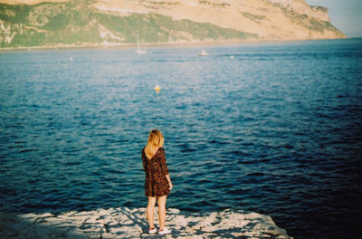 High angle view of woman standing on rock in front of sea