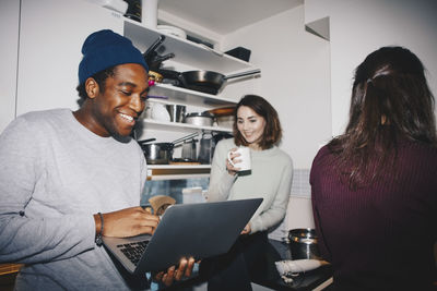 Happy man showing laptop to female friend with coffee cup in kitchen