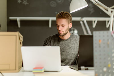 Confident young businessman using laptop while sitting at desk in creative office