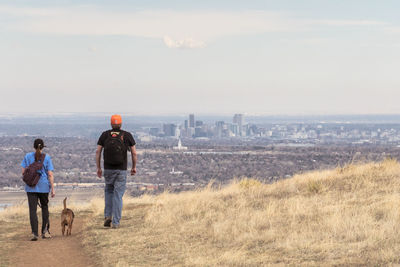 Rear view of man and woman walking with dog on pathway against sky