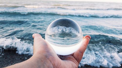 Cropped hand holding crystal ball against sea