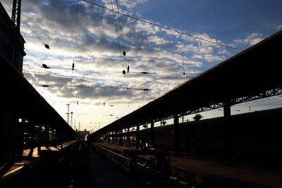 Railroad station platform against sky during sunset