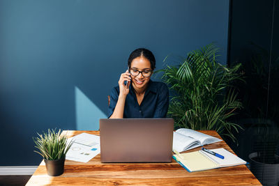 Businesswoman talking on phone while working at table