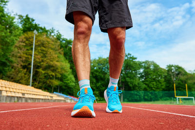 Athlete wearing bright blue running shoes on red stadium track during training