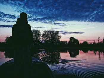 Silhouette man standing by lake against sky during sunset