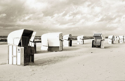 Empty hooded chairs on sand at beach against cloudy sky