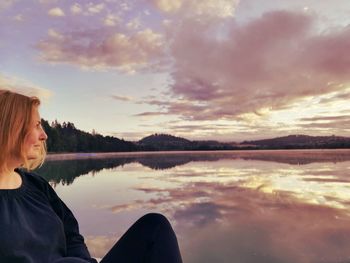 Close-up of woman sitting by lake against sky