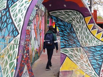 Rear view of man walking against graffiti wall