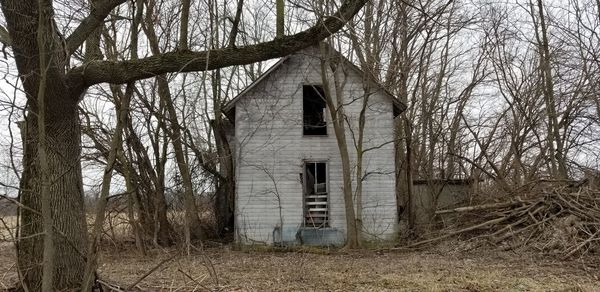 Abandoned building by bare trees against sky