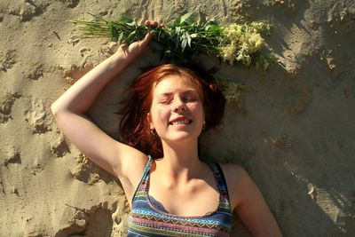 Directly above shot of happy young woman holding plants while lying on sand at beach