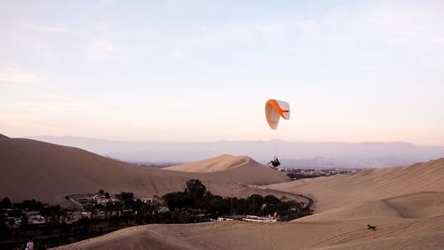 Parapendio flying over desert against sky