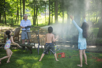 Grandfather spraying water on grandchildren at yard