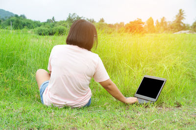 Rear view of woman using laptop while sitting on grassy field