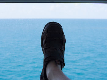 Low section of man wearing footwear against sea