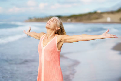 Senior woman with arms outstretched on beach