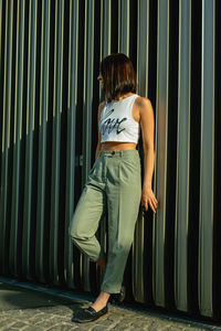 Thoughtful young woman looking away while standing against corrugated iron