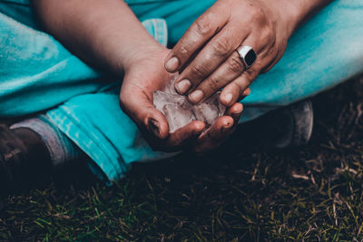 Low section of person holding ice cubes while sitting on grassy field