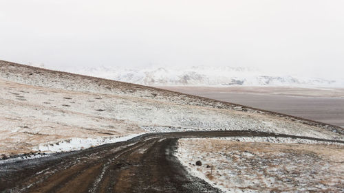 Road on snow covered landscape against sky