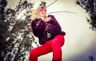 Low angle portrait of young woman against tree