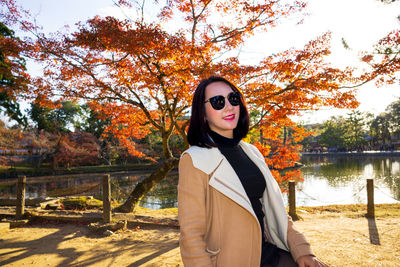 Portrait of young woman standing by lake during autumn