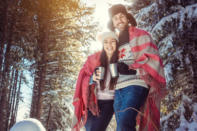 Portrait of smiling young woman standing against trees in winter