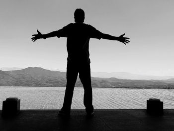 Rear view of silhouette man standing on beach against sky during sunset