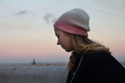Side view of woman wearing knit hat against sky during sunset