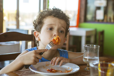 Funny curly-haired boy eating tortellini in restaurant