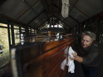 Senior man cleaning wooden boat in a boathouse