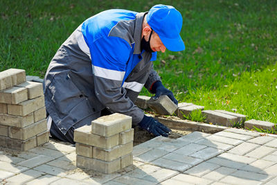 Bricklayer in work clothes sits on sidewalk and lays out paving slabs. sight of working man in open